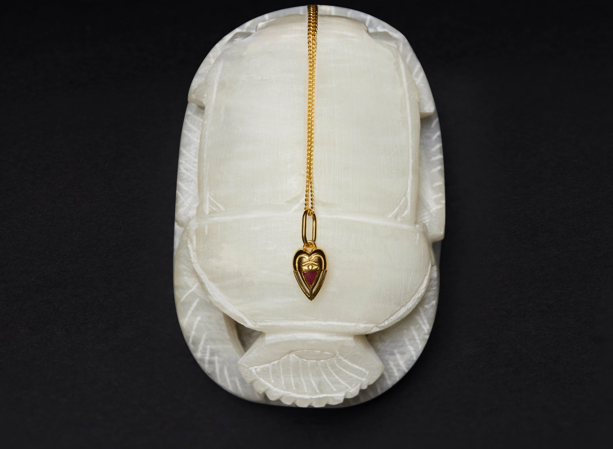 Mini gold Lovers Heart pendant on a white alabaster scarab