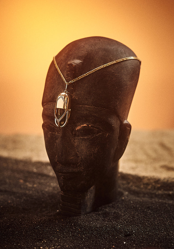 Gold Capsule amulet displayed on an Egyptian sculpted head